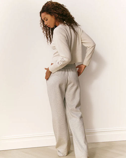 Person standing with their back to the camera, wearing a light-colored long-sleeve top with lace sleeve details and matching soft pants.