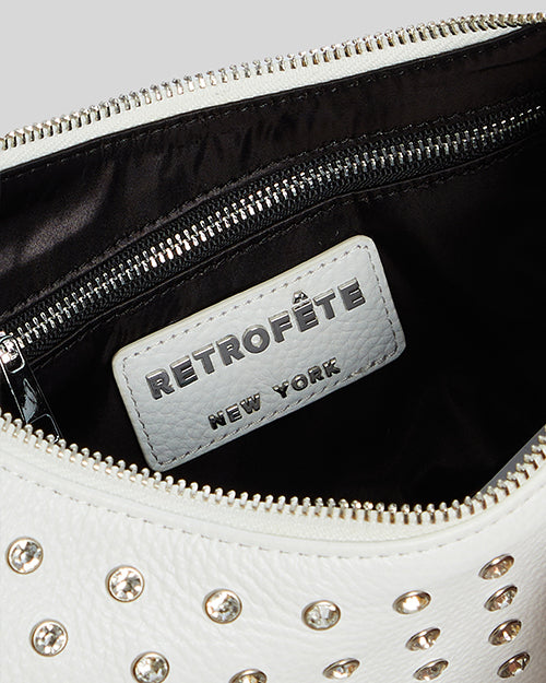 Close-up of a white leather bag with silver stud details. The bag is partially unzipped, revealing a black interior.
