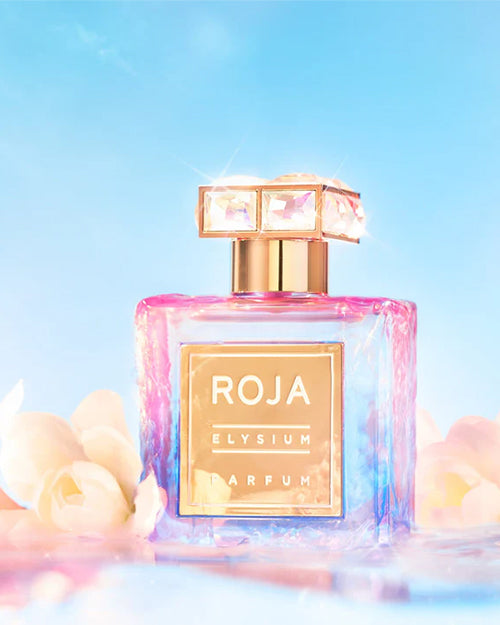 A square perfume bottle with a gradient color, a gold cap with square gem decorations on top, and a gold square label on the front of the bottle reads: "ROJA ELYSIUM PARFUM." The background is white. The bottle is placed in front of a blue sky surrounded by white flowers.