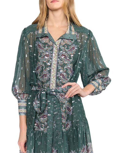 Close up of a person wearing a green long-sleeved dress with a paisley pattern in purple, white, and gold. The dress features a collar, button-down front, a belt tied at the waist, and slightly sheer sleeves with matching patterned cuffs.