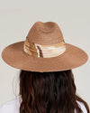 Back view of a person wearing a wide-brimmed brown straw hat with a beige and white patterned band around the crown. Long, wavy hair flows from underneath the hat.