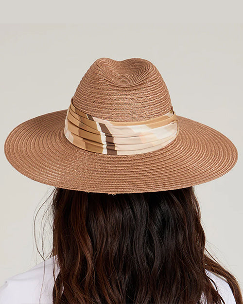 Back view of a person wearing a wide-brimmed brown straw hat with a beige and white patterned band around the crown. Long, wavy hair flows from underneath the hat.