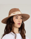 A person with long, wavy brown hair wearing a wide-brimmed, light brown straw hat with a beige ribbon around the crown.