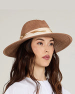 A person with long, wavy brown hair wearing a wide-brimmed, light brown straw hat with a beige ribbon around the crown.
