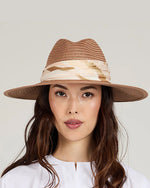 Front view of a woman wearing a brown straw hat with a camouflage band on a light gray background