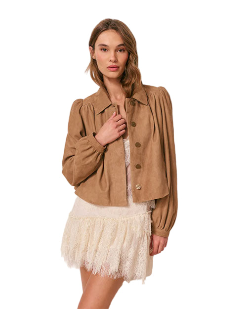 Person wearing a light brown jacket with long sleeves and large buttons over a white lace dress. 