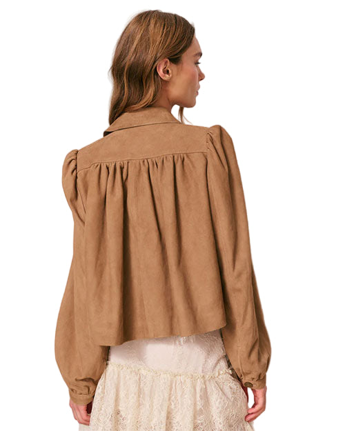 Back view of a person wearing a light brown long-sleeved jacket with gathered fabric details at the shoulders and upper back, paired with a white lace skirt. 