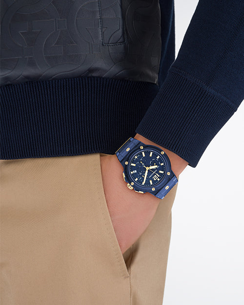 A close up of a person wearing a navy blue watch with gold accents on a white background