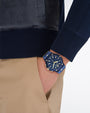 A close up of a person wearing a navy blue watch with gold accents on a white background