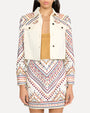 A body shot of a person wearing a yellow shirt under a white denim jacket with intricate, colorful embroidery on the shoulders and sleeves. The jacket has metal buttons and two chest pockets with button flaps, and the model is wearing a matching embroidered skirt.
