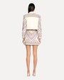 The backside view of a dark-haired person wearing a white denim jacket with intricate, colorful embroidery on the shoulders and sleeves and a matching jean skirt with full embroidery and silver open-toed heels.