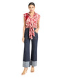 Woman wearing a red floral blouse, blue denim pants and nude heels on a light background