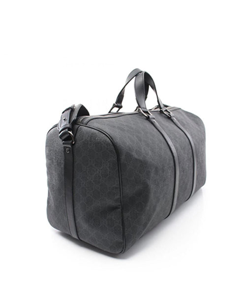 Angle view of a sleek black Gucci duffle bag with a subtle gray pattern, featuring sturdy handles and a versatile adjustable shoulder strap, set against a clean white background.