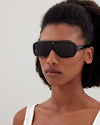 Model wearing black, rectangular-framed Saint Laurent sunglasses with dark lenses. The temples feature the brand name ‘Saint Laurent’. 