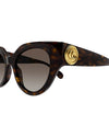 Close-up of tortoiseshell colored, narrow cat-eye sunglasses with brown lenses and gold circular logo on temples.
