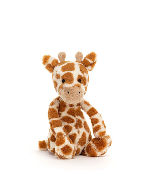 A plush toy giraffe sitting upright. The giraffe has a friendly expression, with brown spots on a cream-colored body, small horns, and eyes.