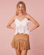 Model wearing a white lace top and a brown pleated skirt, posing against a pink background