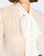 A close-up frontal view of a person wearing a sheer white blouse with a large bow tied at the neck. The tie has a fuller white color.
