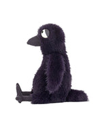 Plush toy resembling a bird with dark purple fur, a large beak, and big white eyes, sitting upright with legs stretched out in front.