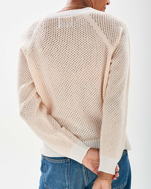 The backside view of a person wearing a light pink V-neck sweater with long sleeves. The sweater has a textured knit pattern and white ribbed cuffs, hem, and neckline. The persons legs are cut out of the image.
