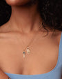 Close-up image of a person wearing a blue top with thin straps, showcasing layered necklaces. Bottom necklace is a key and top necklace charm is a door tag charm with 'do not disturb' on it.