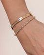 A gold bangle bracelet adorned with cut-out patterns. The word “Love” is engraved on the bracelet, which is further embellished with colorful gemstones of varying sizes and shapes. The bracelet is paired with a different colorful bracelet.