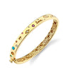 A gold bangle bracelet adorned with intricate cut-out patterns. The word “Love” is engraved on the bracelet, which is further embellished with colorful gemstones of varying sizes and shapes. 