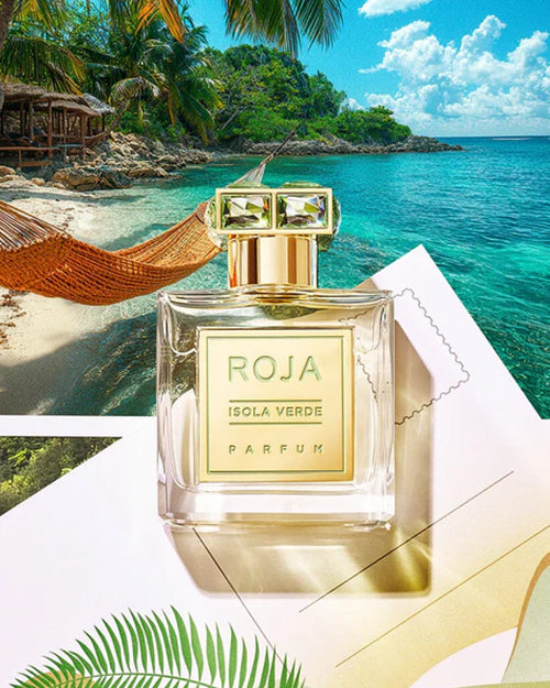 Roja Parfum bottle on a tropical beach with turquoise water and palm trees.