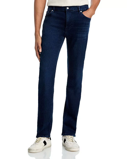 Person standing upright wearing dark blue jeans and white sneakers with black accents, with one hand in the pocket.