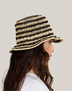 Side view of a woman wearing a black and beige striped bucket hat on a plain background