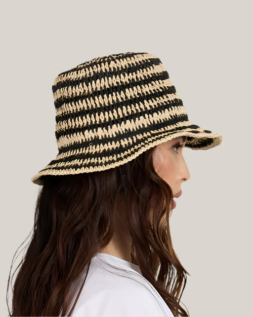 Side view of a woman wearing a black and beige striped bucket hat on a plain background
