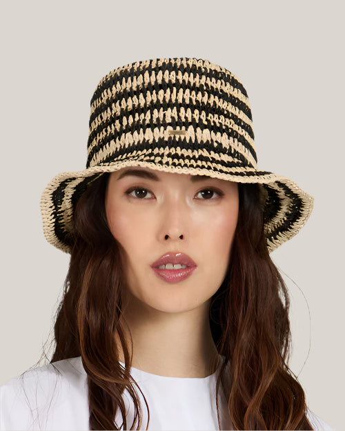 Front view of a woman wearing a black and beige striped straw hat  and a white shirt on a plain background