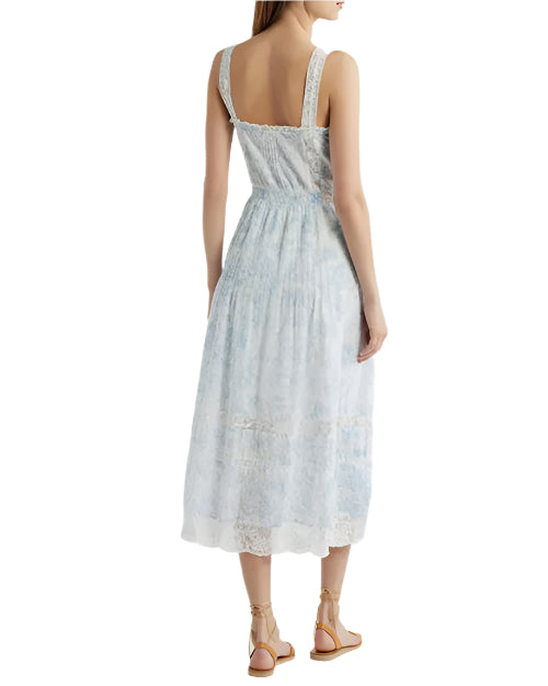 The backside view of a person wearing a light blue and white dress with a half open back and over the shoulder straps. The dress has lace detailing and a fitted bodice that flares out into an A-line skirt. The person is also wearing tan strappy sandals.