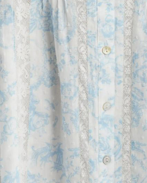 An extremely close-up view of the fabric on a light blue and white dress. The dress has a light blue floral pattern and is buttoned down the front with small buttons. The dress features vertical pleats along the front. There are lace details running vertically alongside the pleats
