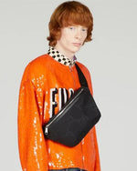 Black Gucci belt bag worn but a person wearing an orange jacket. Belt bag is worn across the chest.