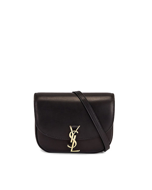 A black leather shoulder bag with a curved bottom, flap top, and a gold-toned metal logo resembling the letters ‘YSL’ intertwined on the front. The bag has a streamlined, elegant design with a single strap for carrying over the shoulder or across the body. 