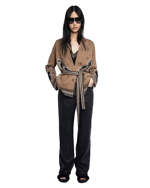 Person standing and wearing dark sunglasses, a brown cardigan with black and white patterns, tied at the waist with a matching belt, paired with black pants and black open-toe shoes.