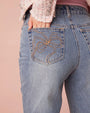 A close-up on the left pocket on jeans with a brown bow stitching.