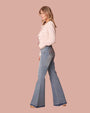 Side view of model in high-waisted flared jeans in classic blue denim wash, featuring a snug fit that flares into a stylish bell-bottom shape. Paired with brown heeled shoes and pink tweed jacket.