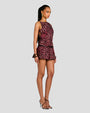 An angled sideview of a brunette model wearing a sleeveless dress with a slightly open-back, a maroon and black leaf pattern, and a fitted bodice and a flared skirt with a black belt. She is also wearing gold hoop earrings, bangles, and black open-toed heels.