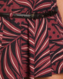 A close-up image of a model wearing a frilled skirt featuring a maroon and black leaf pattern, and a black belt featuring a martini glass shaped belt buckle.