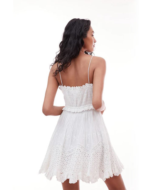 Model showing the back of the dress. wearing a white, sleeveless dress with intricate lace and pleated details, standing against a plain background.