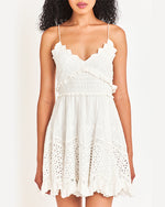Model wearing a white, spaghettis strap dress with intricate lace and pleated details, standing against a plain background.