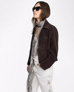 Woman wearing a brown jacket, white pants, and sunglasses on a white background