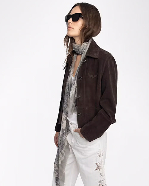 Woman wearing a brown jacket, white pants, and sunglasses on a white background