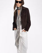 Person wearing a brown jacket, white pants, and a long scarf on a white background