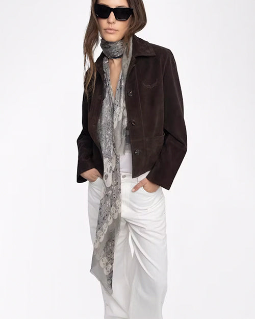 Person wearing a brown jacket, white pants, and a long scarf on a white background
