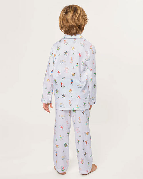 Child standing barefoot with their back to the camera, wearing a light-colored pajama set with long sleeves and pants, decorated with small, colorful illustrations, against a plain background.