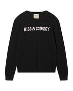Black sweater with white capital text 'KISS A COWBOY' across the chest and a neckline label reading 'Jumper 1234'