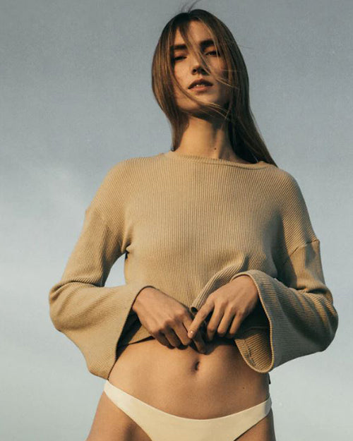 Person wearing a crop bell long sleeve sweater with a matching color swimsuit bottoms.